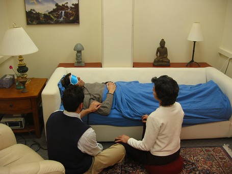 En person som behandlas med psykedelika (psilocybin) i en soffa med ögonbindel och hörlurar med två terapeuter/psykologer